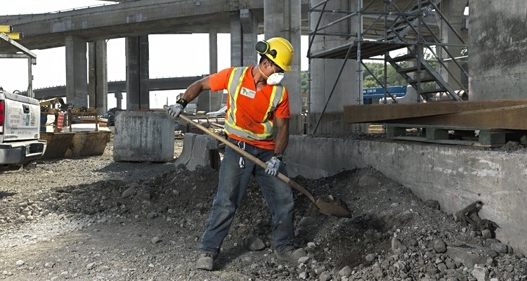 Worker shovelling concrete wearing a 3M™ Particulate Respirator